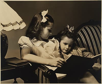 Anton BRUEHL | not titled [Two girls sitting on a sofa looking at a book]