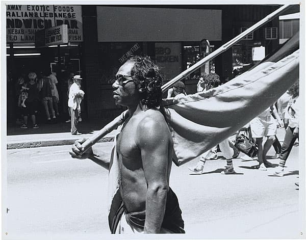 Michael RILEY | Dawson Drew [man carrying flag in street march], c. 1983